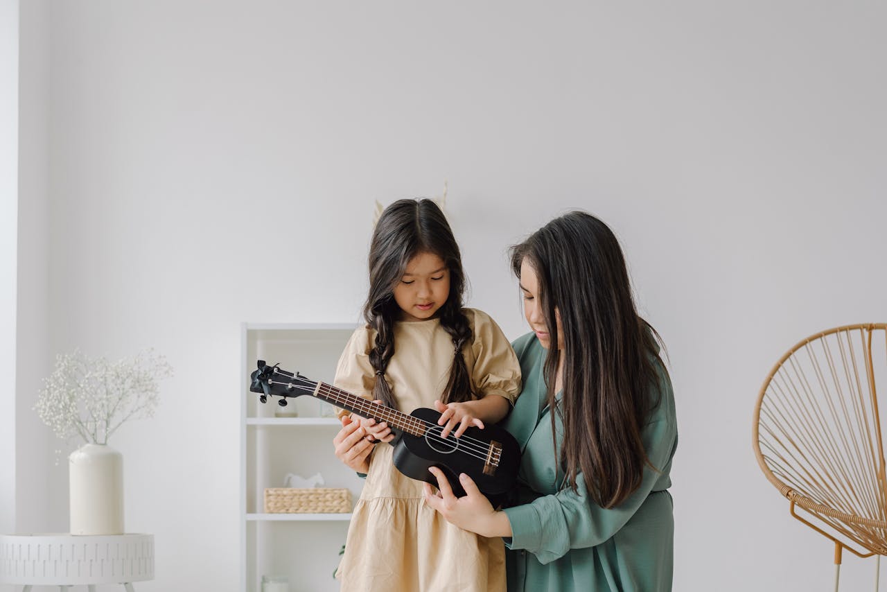 A woman teaching her daughter to play the ukulele in a cozy home setting with natural light.